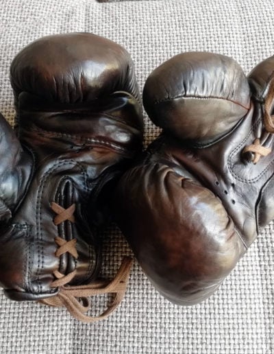 A pair of vintage John Woodbridge brown boxing gloves on a sofa