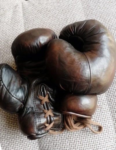 A pair of vintage John Woodbridge brown boxing gloves lying on a sofa in the light