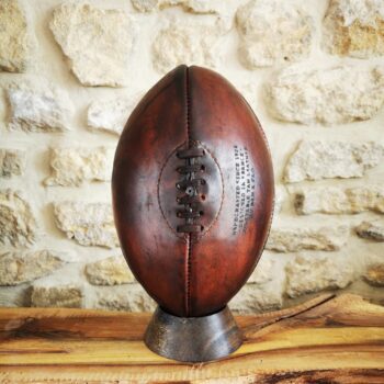 Ballon de rugby vintage marron exposé sur son socle en chêne massif exotique.