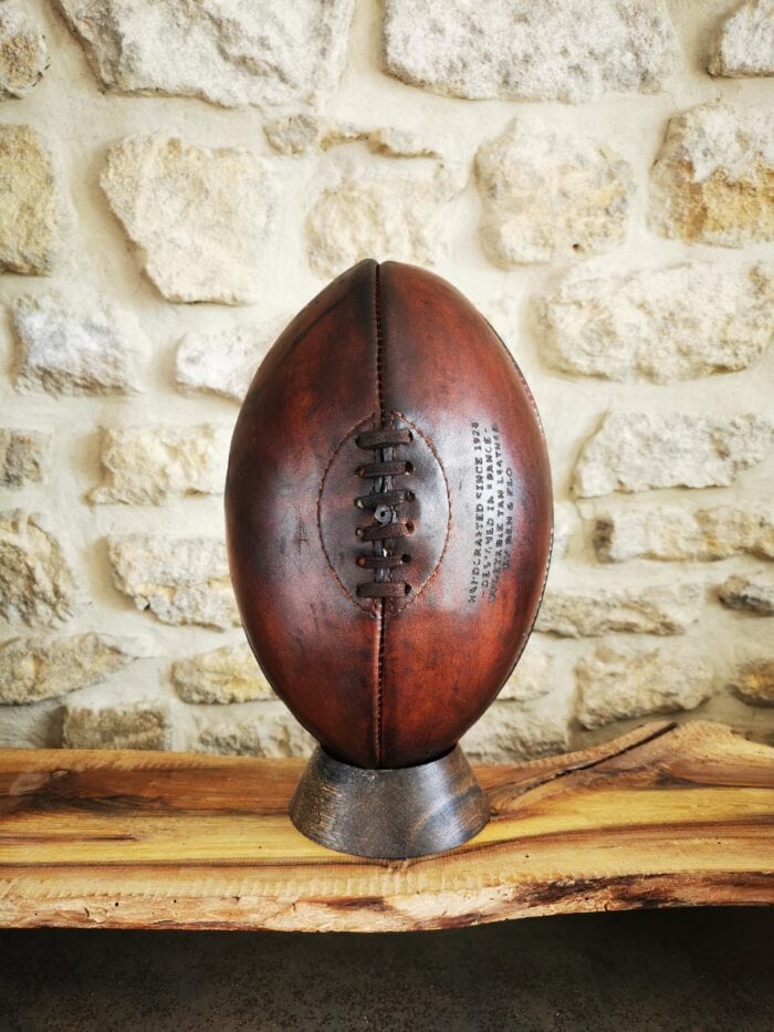 Ballon de rugby vintage marron exposé sur son socle en chêne massif exotique.