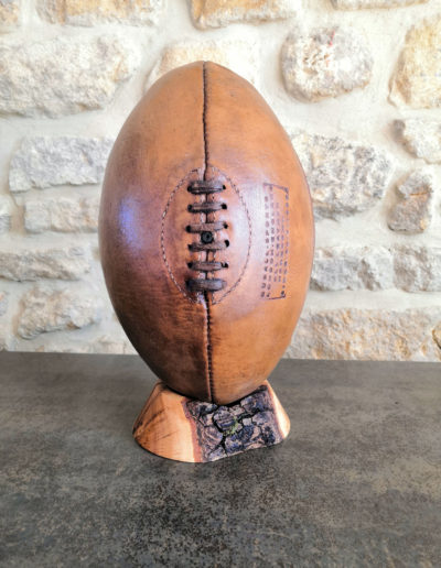 An old havana brown coloured rugby ball presented on its wooden base