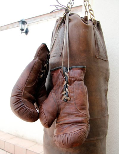 Old brown boxing gloves hanging from a large punching bag outside