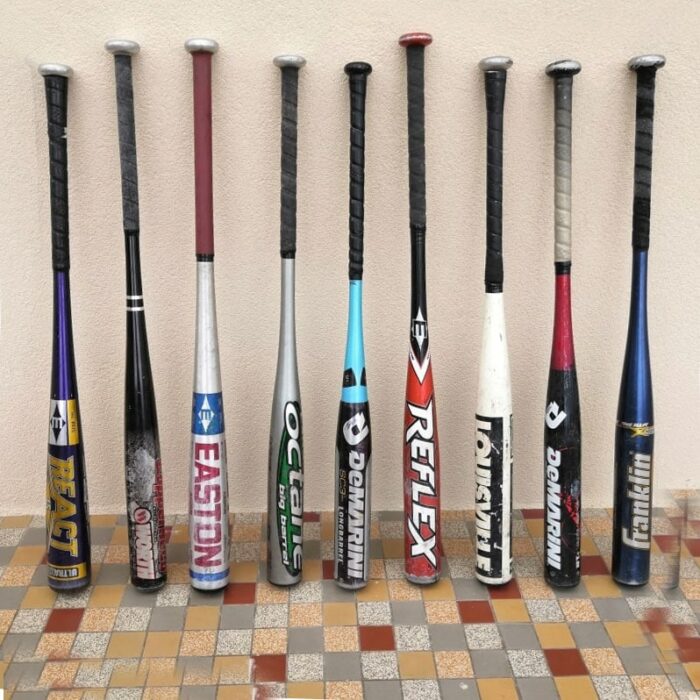 9 antique aluminum baseball bats standing against a wall