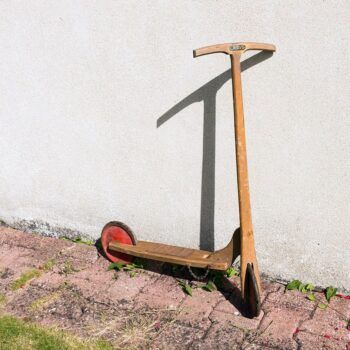 Ancienne trottinette en bois vintage posée contre un mur