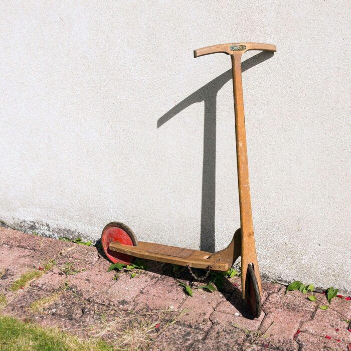 Ancienne trottinette en bois vintage posée contre un mur