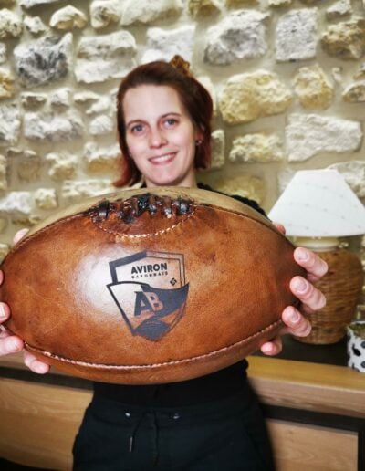 Une femme tiens un ballon de rugby vintage avec le logo de l'Aviron Bayonnais Rugby pro dessus.