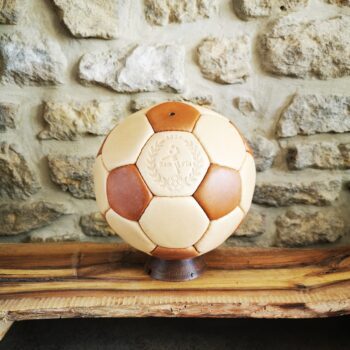 Ballon de handball en cuir beige et marron exposé sur son socle en bois