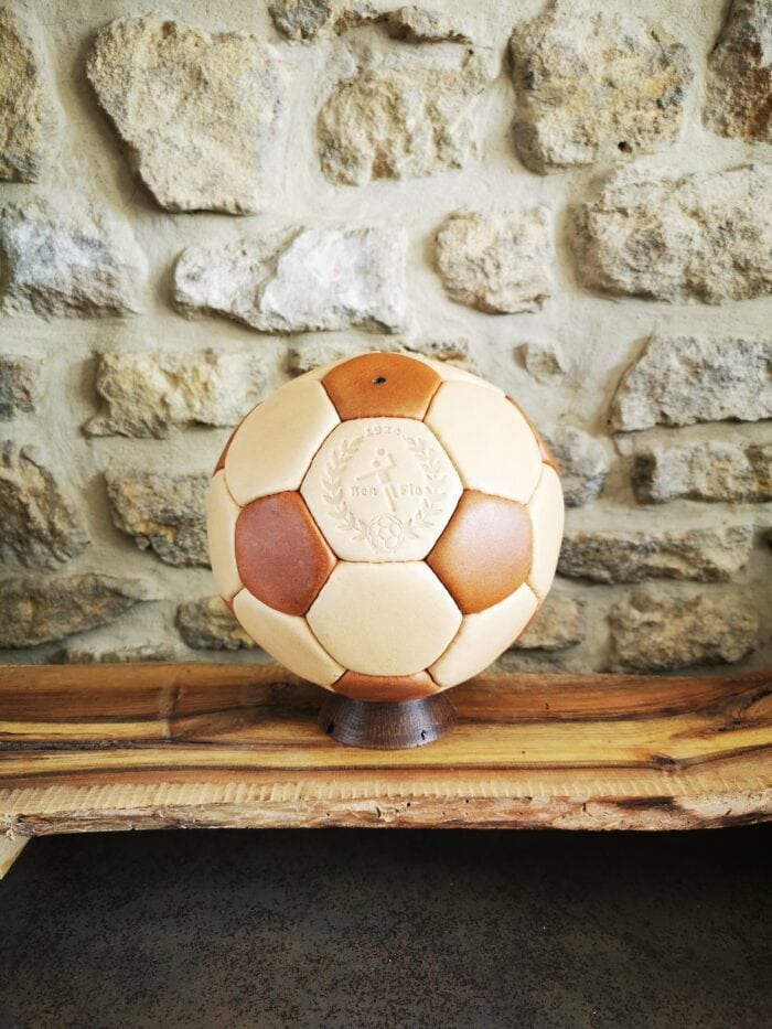 Ballon de handball en cuir beige et marron exposé sur son socle en bois