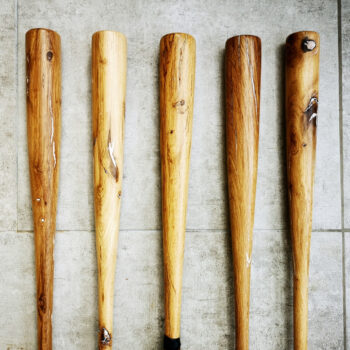 5 battes de baseball en bois vintage posées sur du carrelage gris