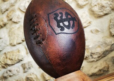 Un magnifique ballon de rugby vintage marron avec le logo du stade toulousain pris en perspective sur un socle en bois.