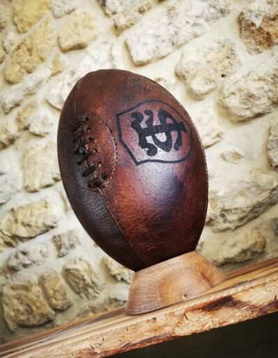 Un magnifique ballon de rugby vintage marron avec le logo du stade toulousain pris en perspective sur un socle en bois.