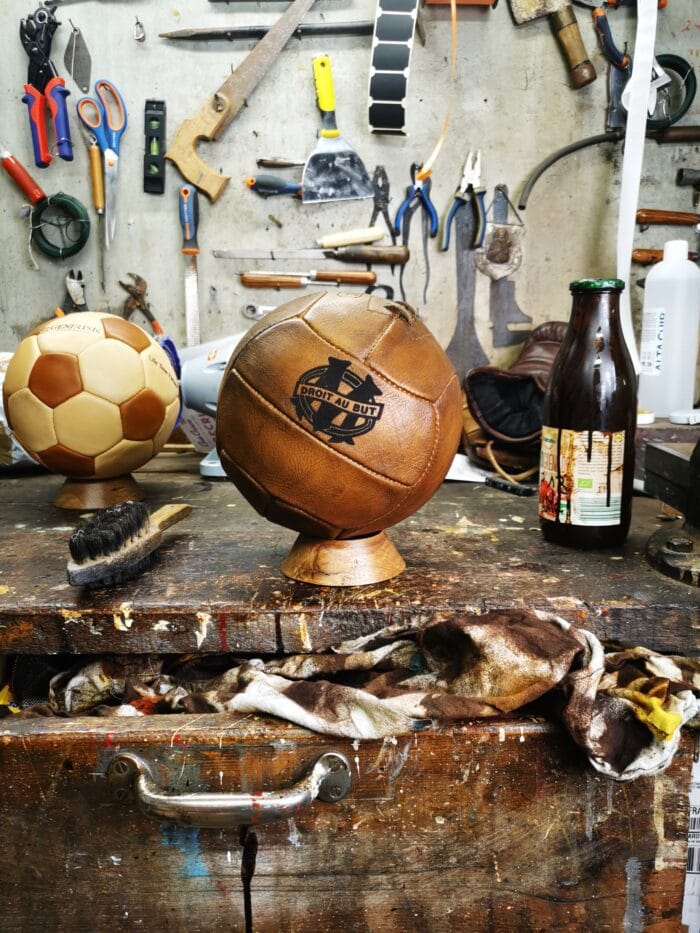 Un magnifique ballon rustique de l'Olympiqe de Marseille posé sur un socle dans un atelier ancien.